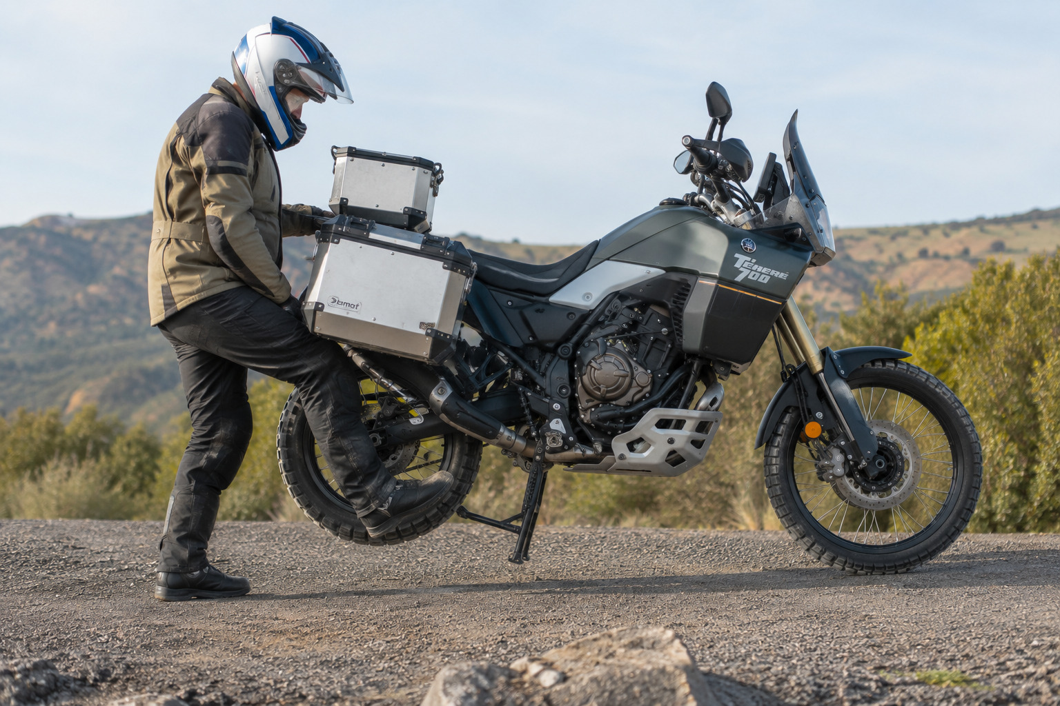 photo en situation réelle d'un motard en train de lever sa moto trail sur béquille centrale